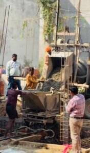 Construction site workers pouring concrete mix from a machine into a footing structure during foundation work.