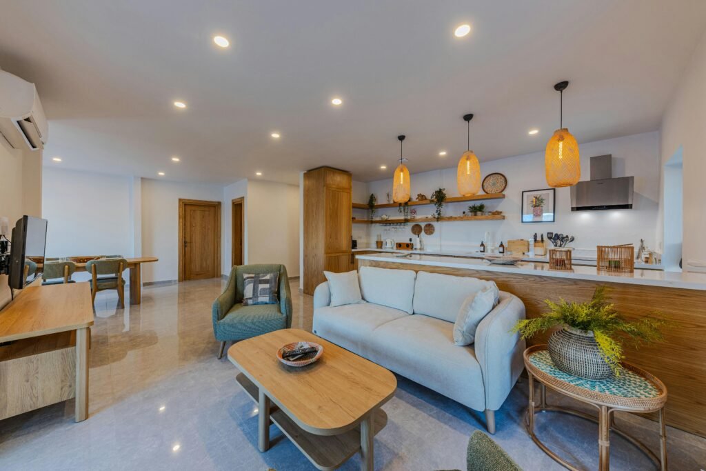 Modern open-plan living room with wooden furniture, comfortable sofa, pendant lighting, and integrated kitchen island design.